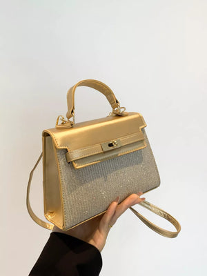 Gold glitter textured mini crossbody bag with top handle and turn-lock closure.