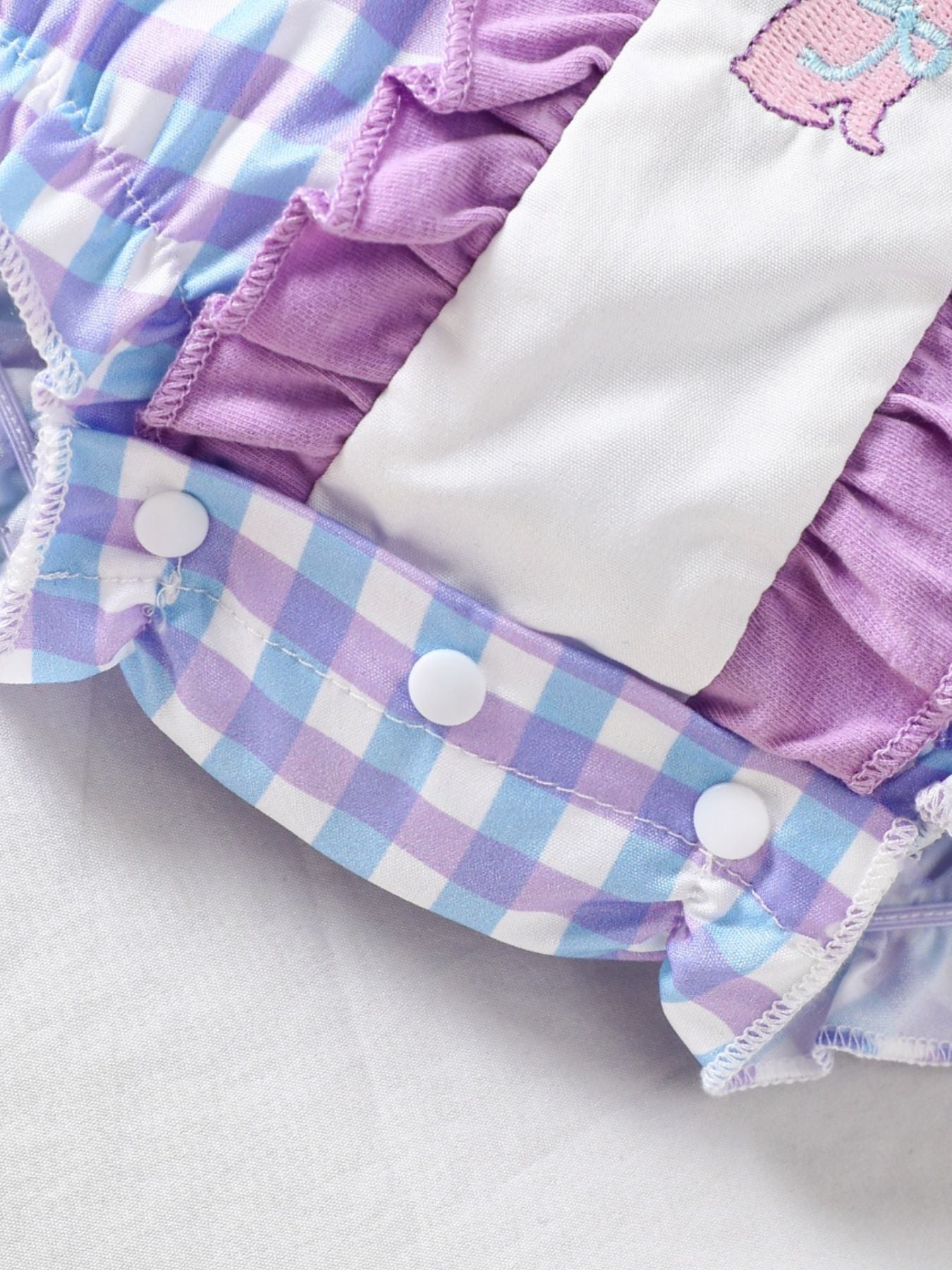 Baby one-piece with pink purple gingham, ruffles, and embroidered bunny detail.