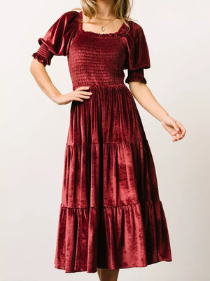 Burgundy velvet midi dress with smocked bodice, square neck, and ruffled puff sleeves.
