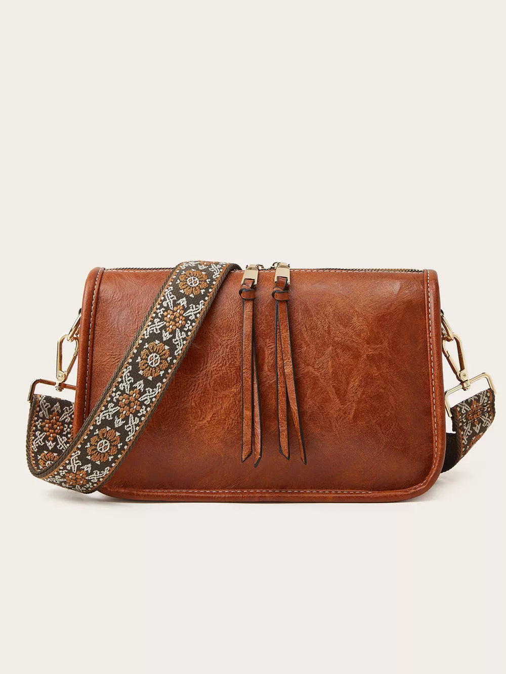 Tan leather crossbody bag with a patterned strap and fringe detail.