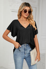 Black eyelet tie-neck blouse with flutter sleeves and a v-neckline.