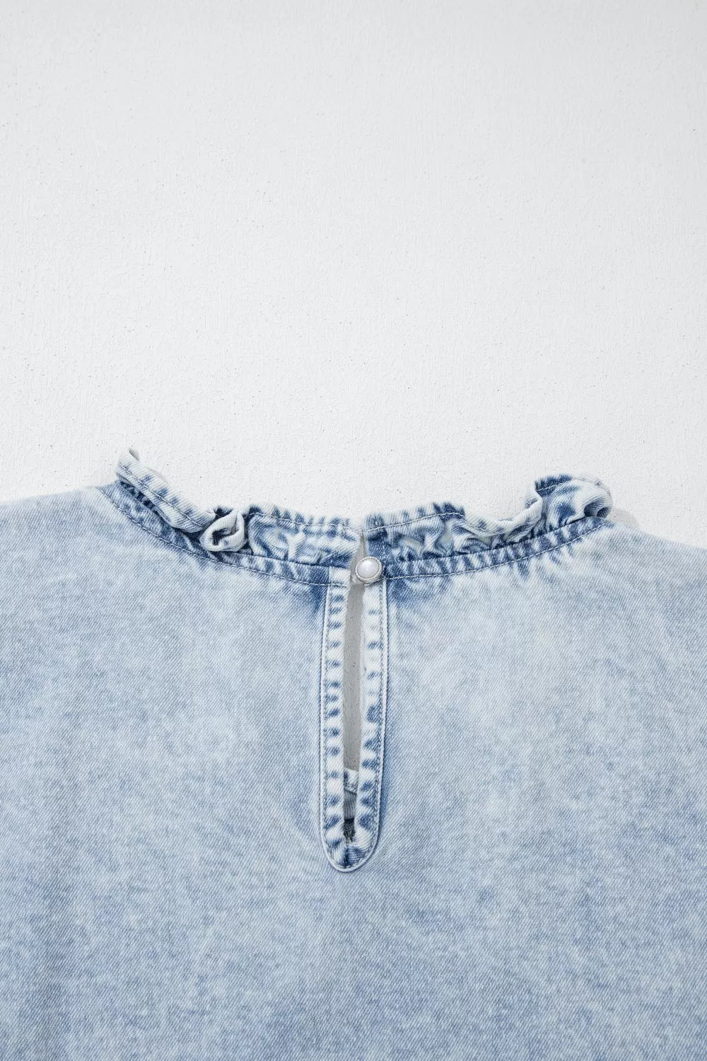 Light wash denim top with ruffled neckline and pearl button back closure