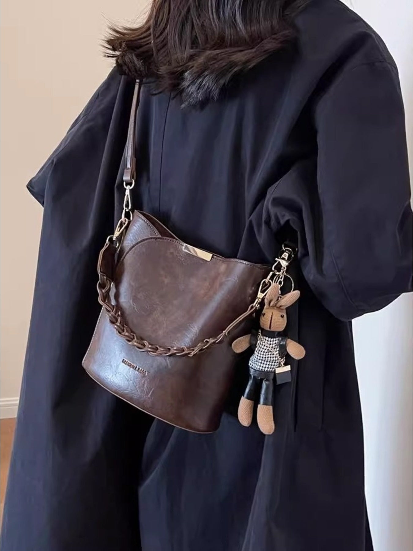 Brown braided bucket crossbody bag with chain detail and bunny charm