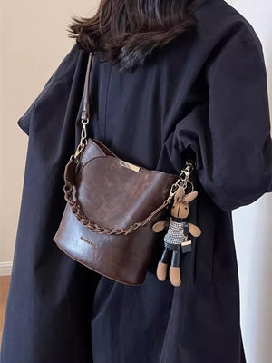 Brown braided bucket crossbody bag with chain detail and bunny charm