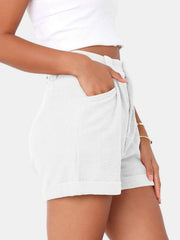 White corduroy pleated high-waist shorts with cuffed hem and pockets.