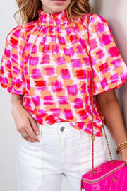 Brushstroke print blouse with ruffled neckline and short sleeves in red, pink, and orange.