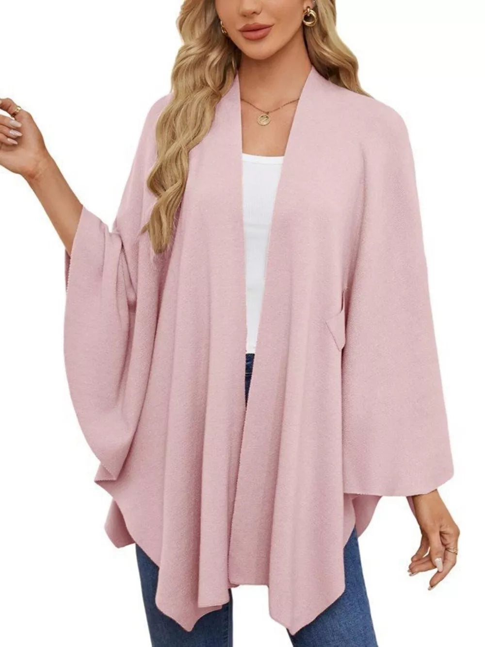Pink knit cape top with draped elegance and wide sleeves, worn over a white tank.