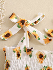 Baby jumpsuit with smocked bodice, sunflower print, and tie straps.