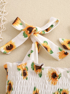 Baby jumpsuit with smocked bodice, sunflower print, and tie straps.