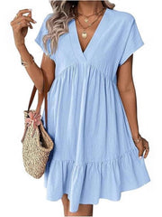 Sky blue ruffled mini dress with V-neck and short sleeves, styled with layered necklaces and a straw bag.