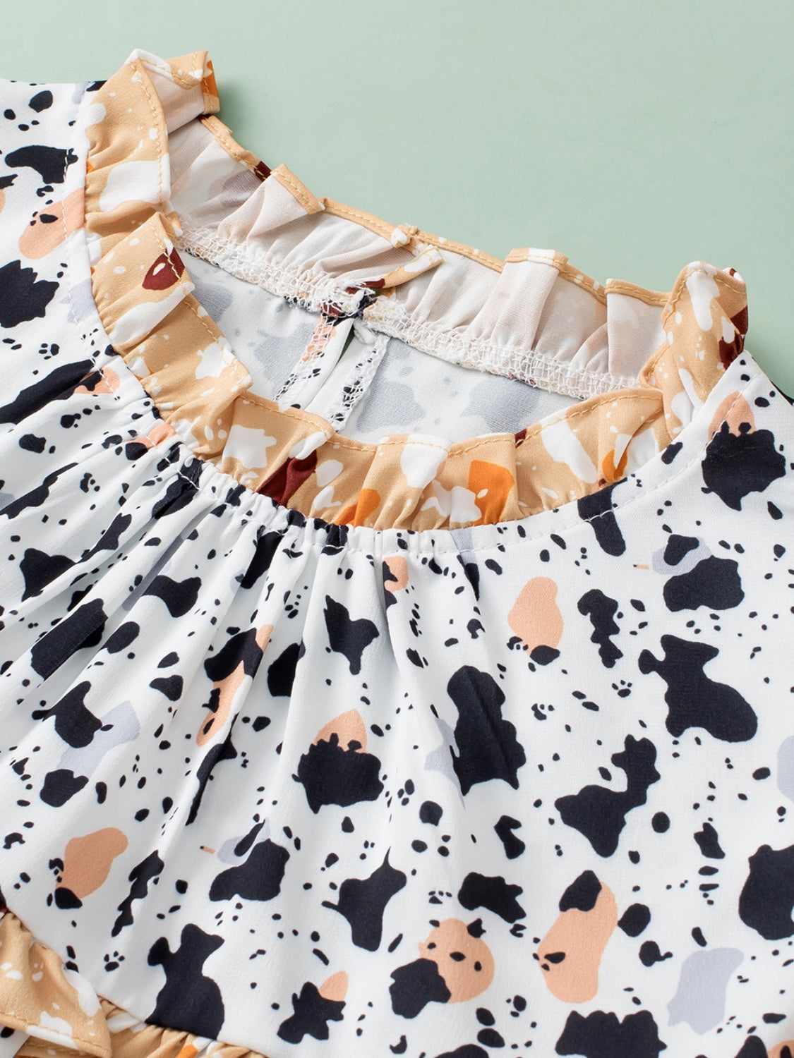 White blouse with terrazzo print, ruffle neckline, and gathered yoke detail.