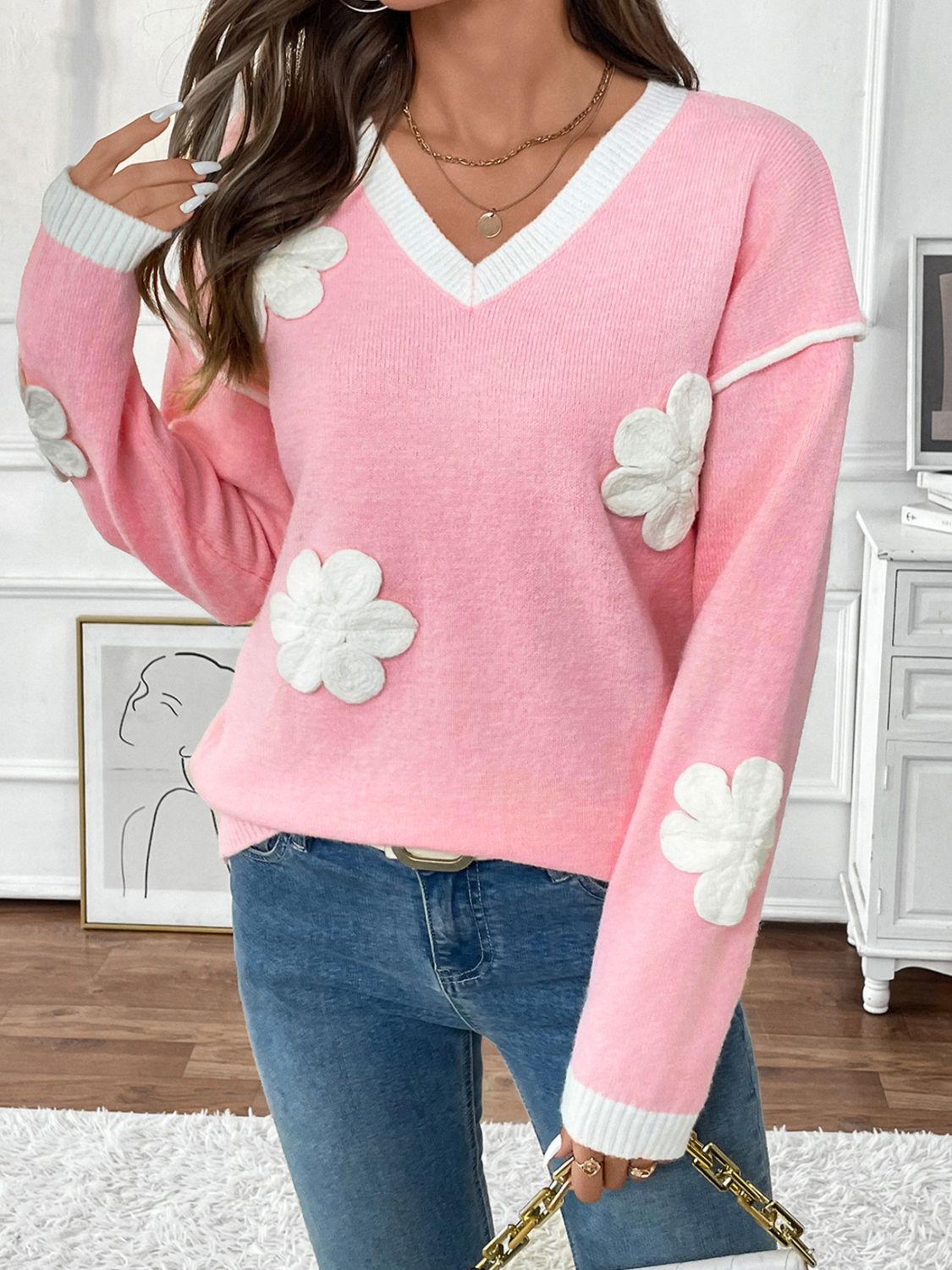 Pink V-neck knit sweater with white floral appliqués and contrast trim.