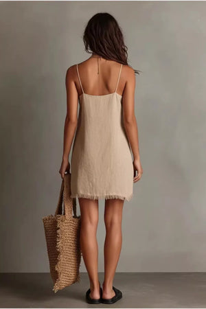 Beige cotton cami dress with fringe hem and V-neck, styled with a straw tote bag.