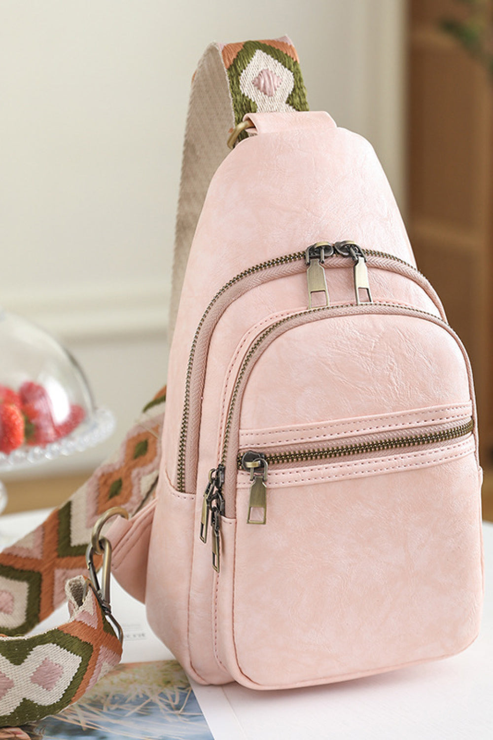 Blush pink geometric strap sling bag with multiple zippered compartments.