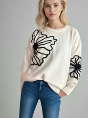Cream knit sweater with black floral embroidery on the front and sleeve.
