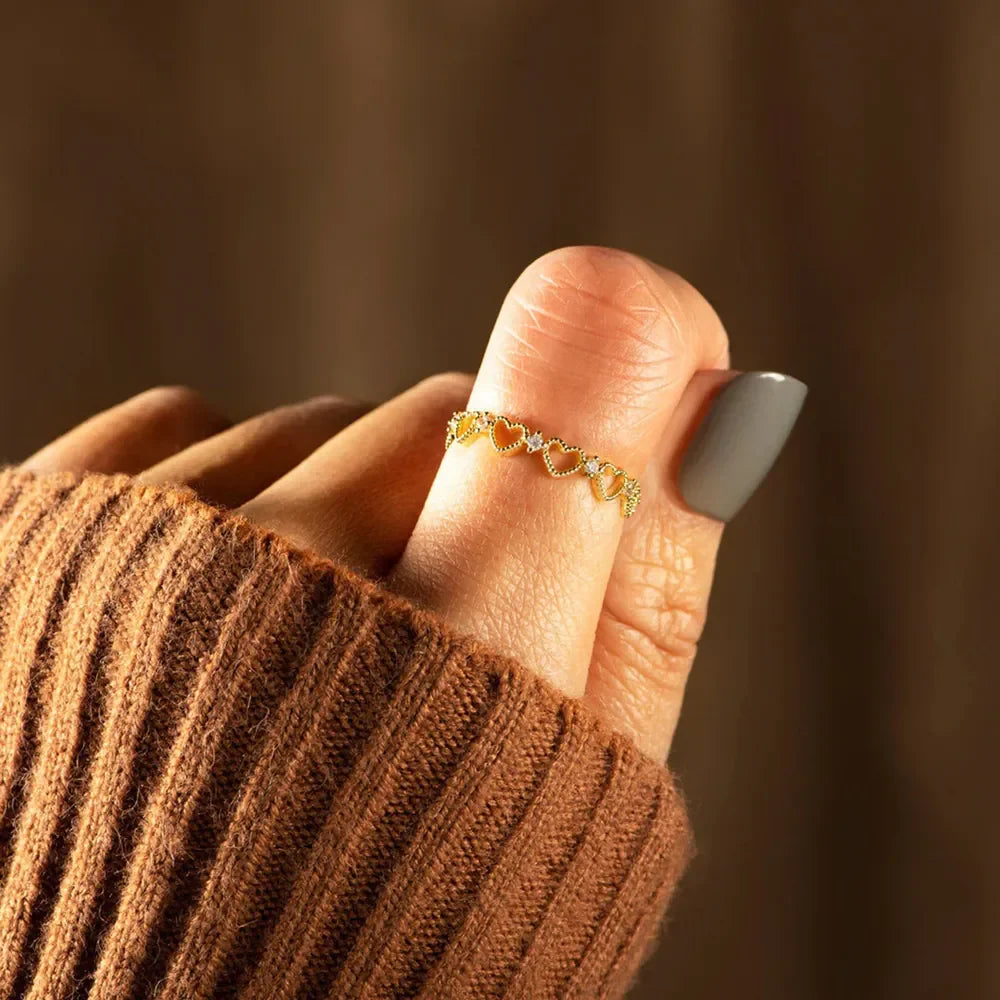 Gold ring with heart pattern and pavé details on a finger.