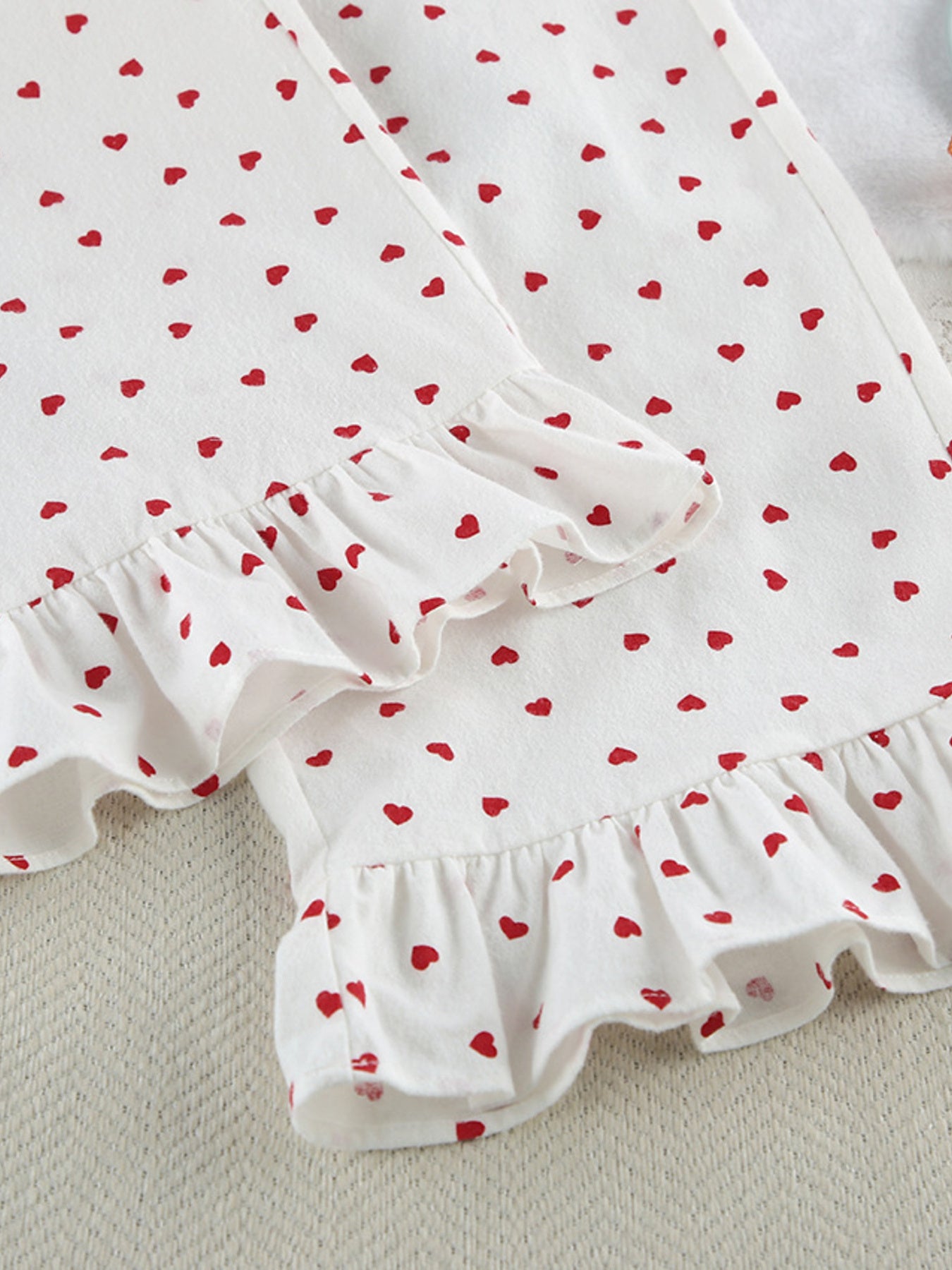 White cotton pajama set with red heart pattern and ruffled trim.