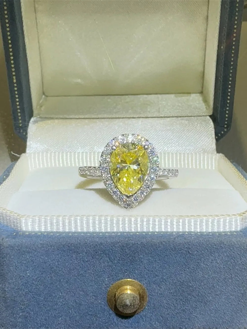 Yellow pear-cut moissanite ring with diamond halo in a jewelry box.