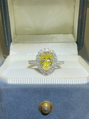 Yellow pear-cut moissanite ring with diamond halo in a jewelry box.