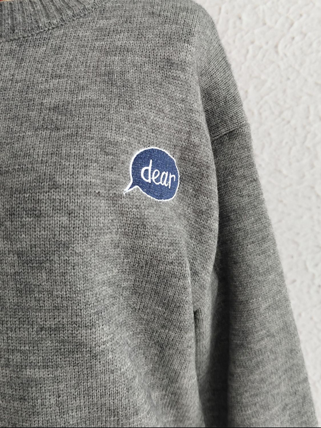 Dark gray acrylic knit sweater with embroidered "dear" speech bubble detail on chest.