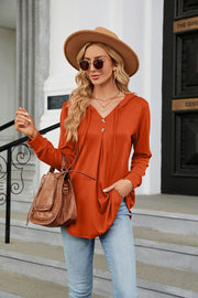 Orange hooded henley top with button placket and drawstring, long sleeves, and a relaxed fit.