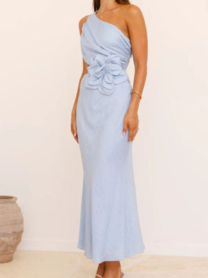 Blue one-shoulder maxi dress with floral appliqué cutout detail and draped bodice.