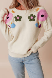 Cream knit sweater with embroidered floral appliqués and tassels.