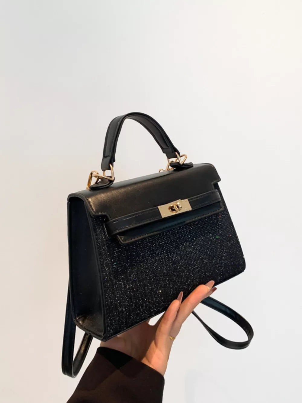 Black glitter textured mini crossbody bag with top handle and gold clasp.