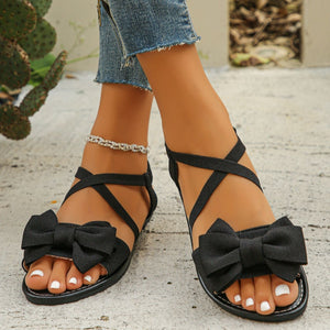Black crisscross bow sandals with ankle straps and a flat sole.