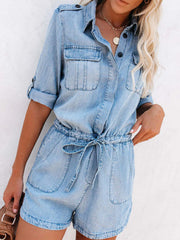 Light denim romper with shirred waist and tie, button front, chest pockets, and cuffed sleeves.