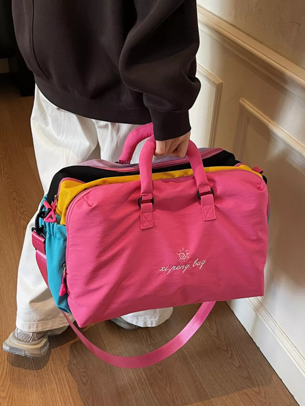 Vibrant pink duffel bag with embroidered logo and multi-color striped accents.