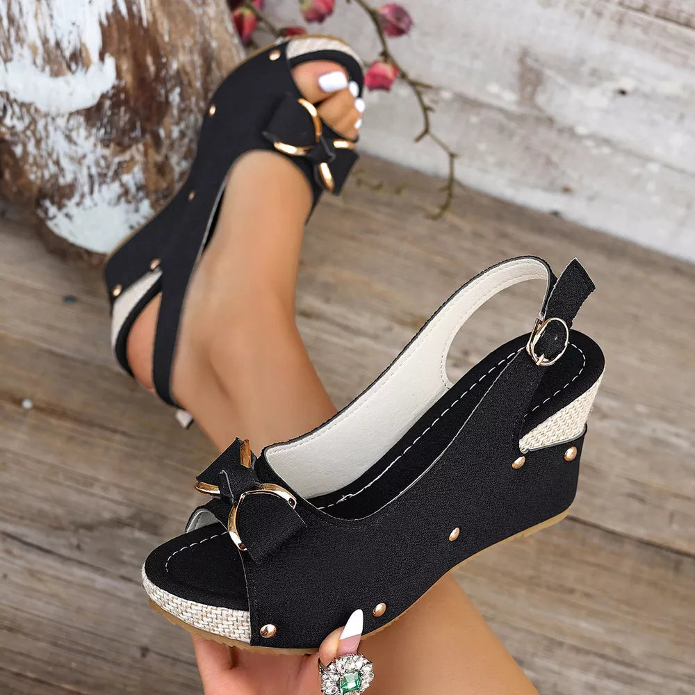 Black peep toe wedge sandals with decorative bow and adjustable strap.