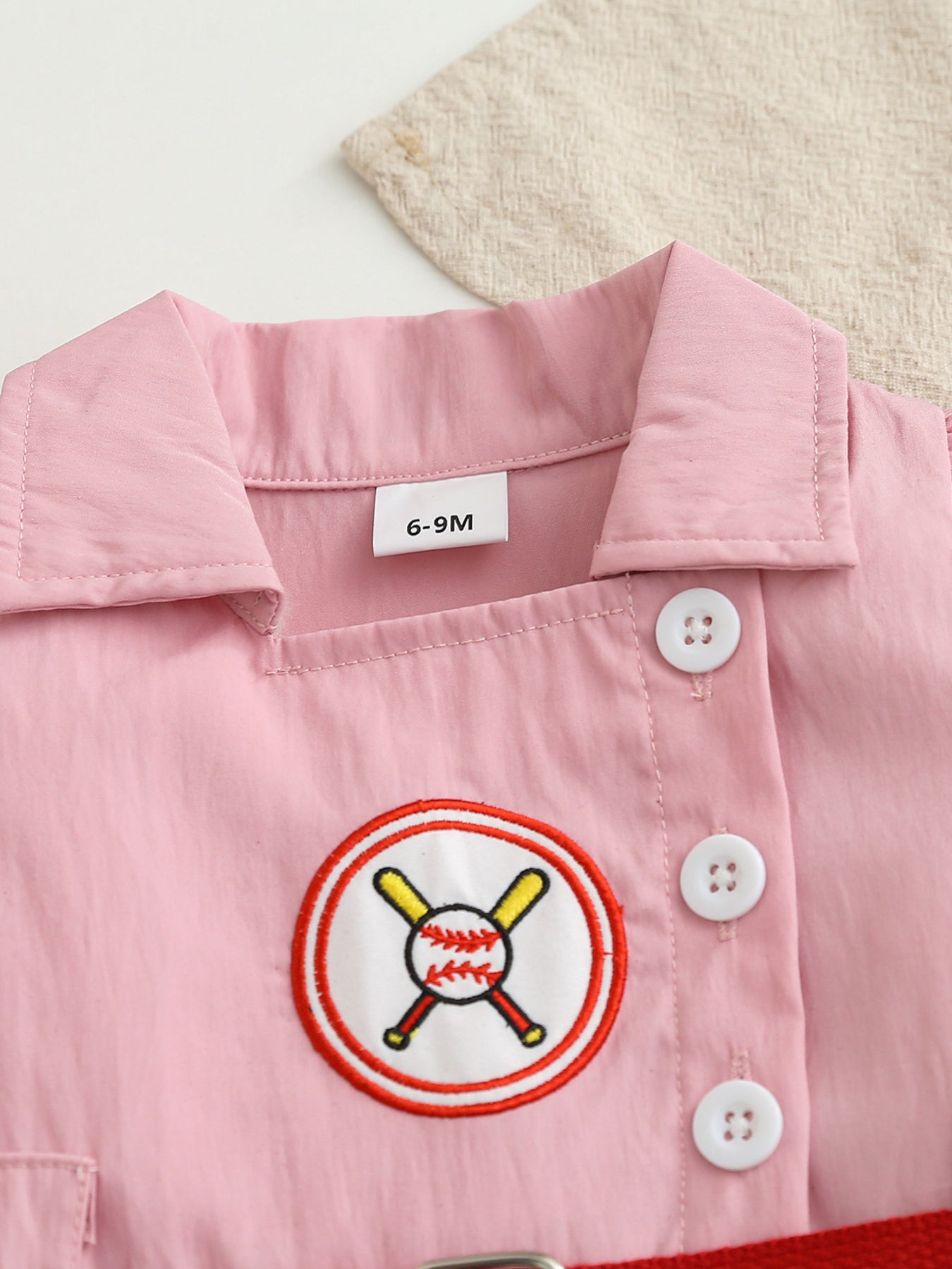 Pink cotton blend baseball dress for baby girls with embroidered baseball patch and white buttons.