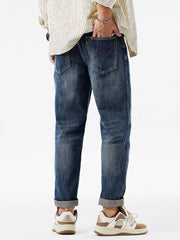 Men's dark blue distressed denim jeans with cuffed hems and zigzag stitching detail on back pocket.
