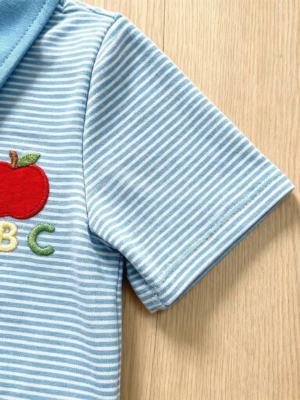 Baby blue striped polo shirt with apple and ABC embroidery detail.