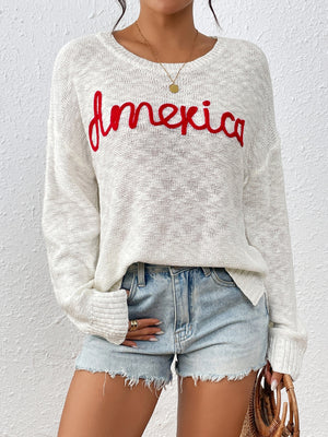 Ivory knit sweater with red embroidered "America" text, crew neck, long sleeves.