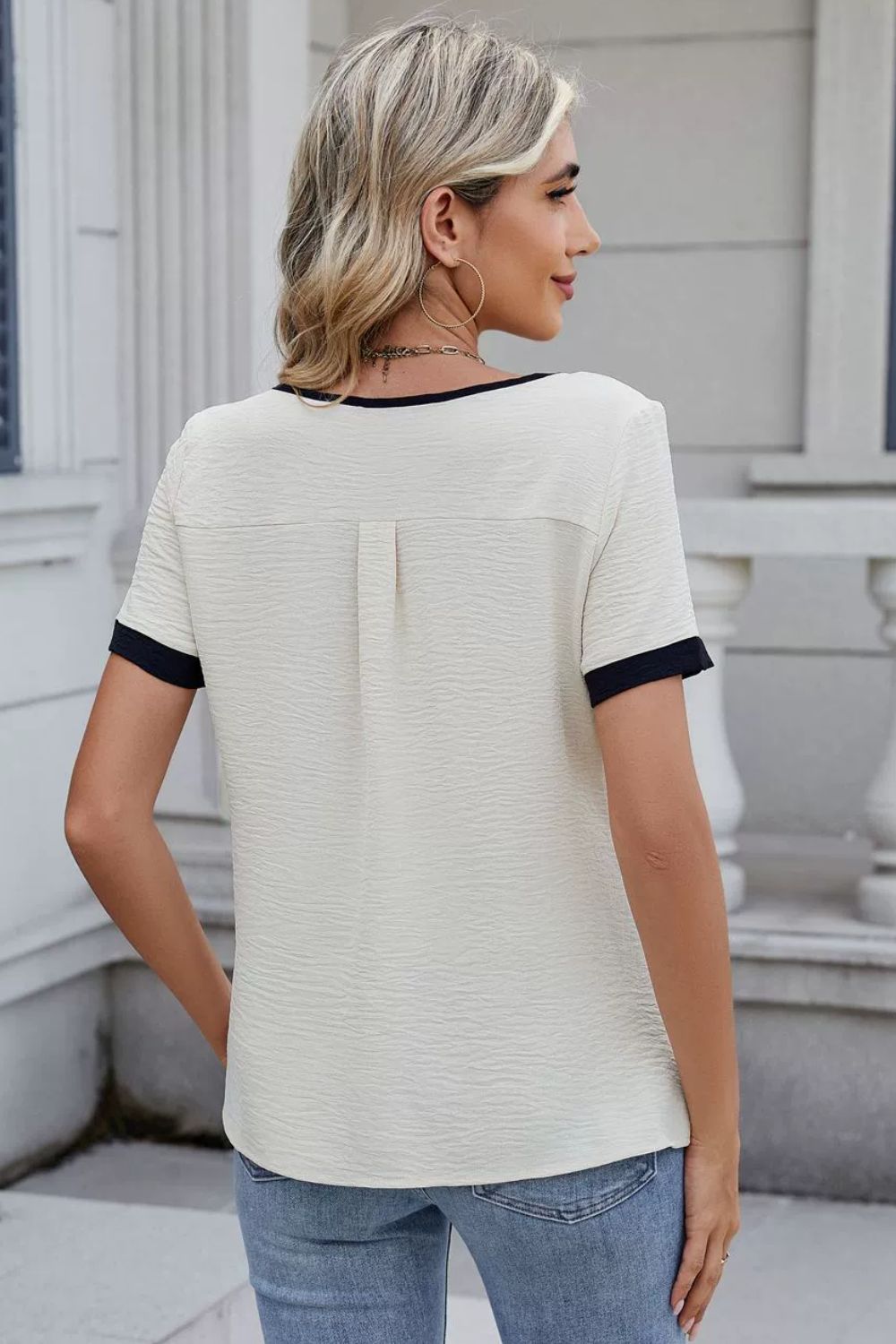 Textured cream blouse with dark navy contrast trim on neckline and sleeves.