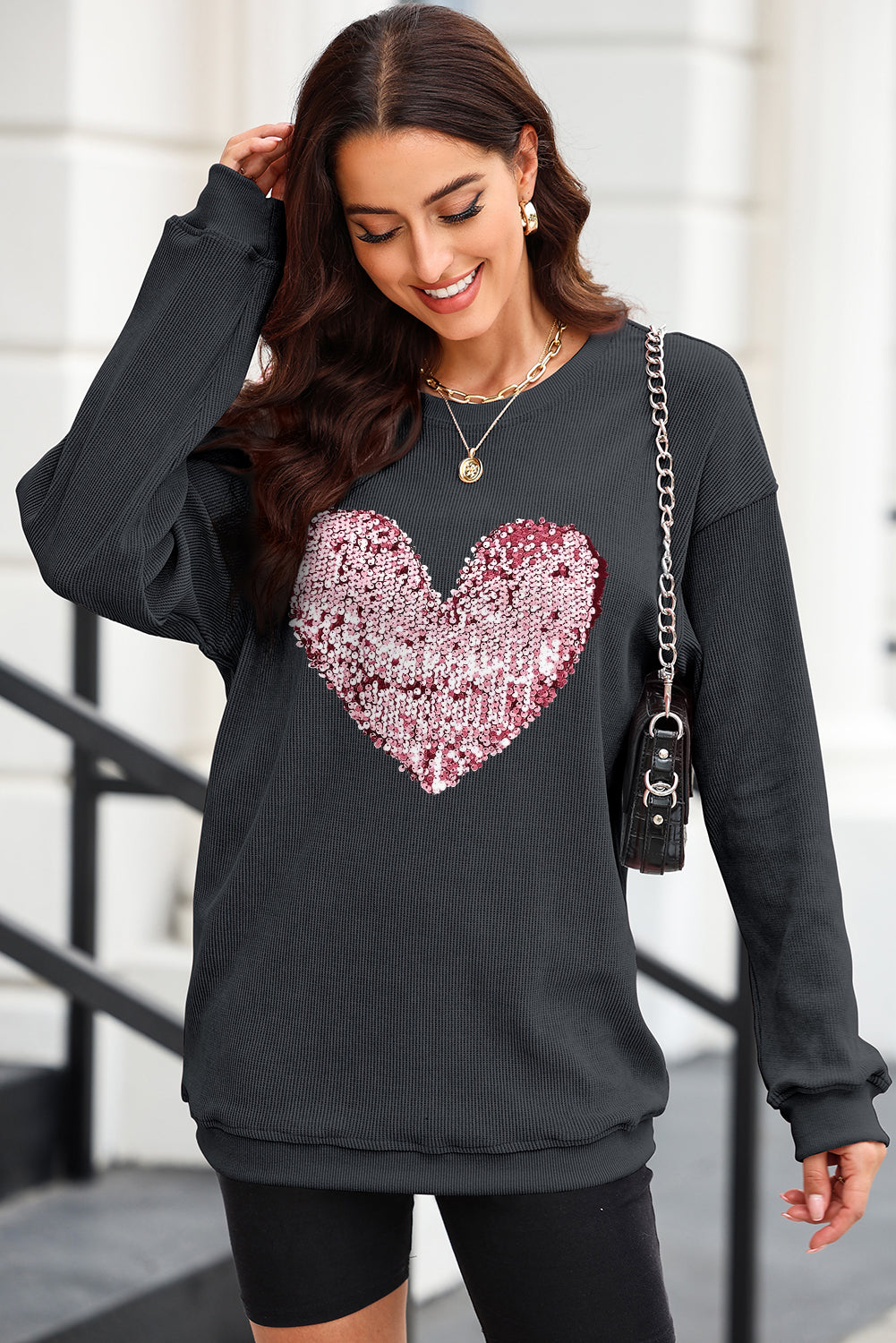 Black ribbed knit sweatshirt with a pink and white sequin heart detail.