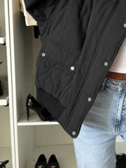 Black quilted bomber jacket with rounded sleeves and snap button pockets.