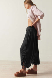 Black gathered ankle-tie balloon trousers with drawstring waist and ruched detailing.