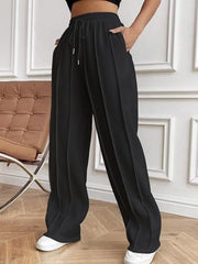 Black pleated wide-leg lounge trousers with drawstring waist and pockets.