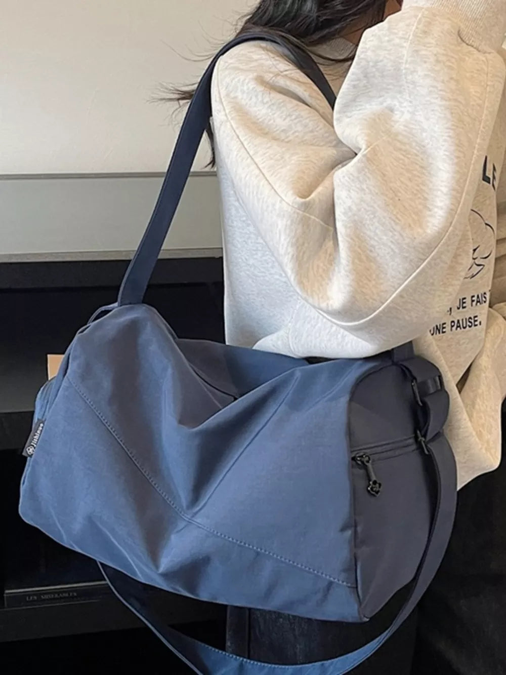 Blue Oxford cloth travel bag with adjustable strap and zippered pocket.