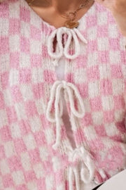 Blush pink and white checkered knit cardigan with tie-front detail and ruffle sleeves.