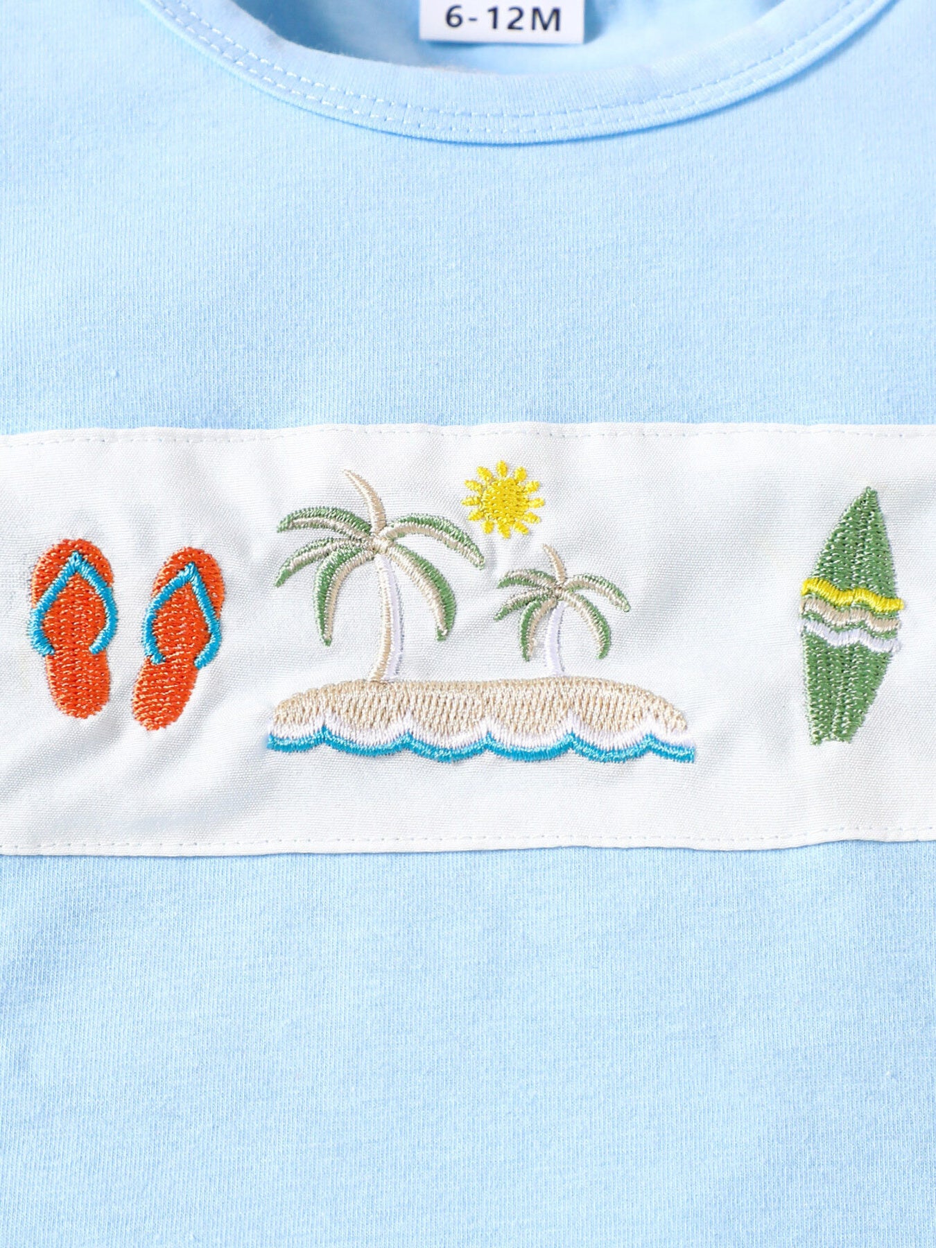 Baby blue cotton t-shirt with embroidered beach scene, flip flops, palm trees, sun, and surfboard.