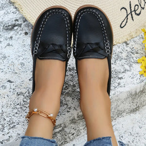 Black leather loafers with white stitching and braided detail.