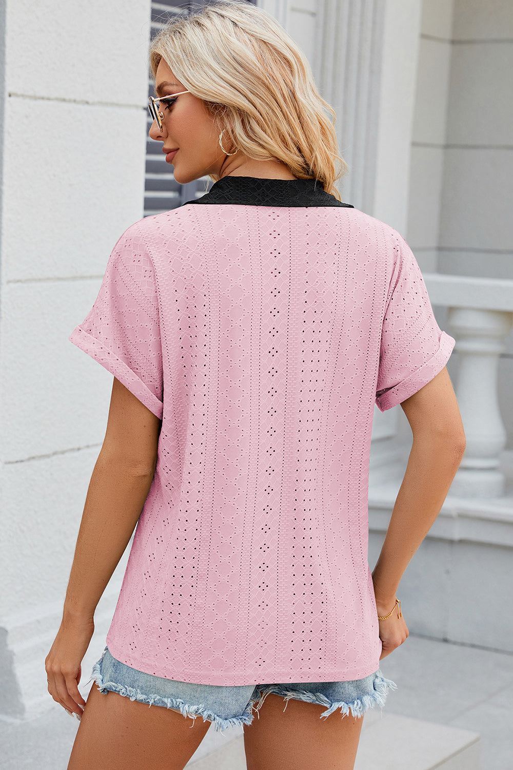 Blush pink perforated polo top with short sleeves and black collar detail.