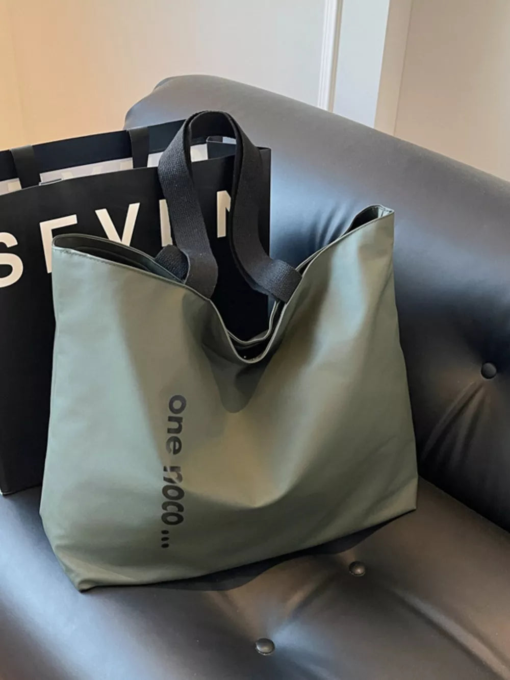 Green minimalist large shoulder bag with black text detail and black straps.