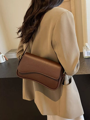 Sleek faux leather crossbody bag in coffee color with a curved flap closure.