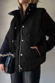 Black quilted stand-collar utility gilet with snap and zip closure.