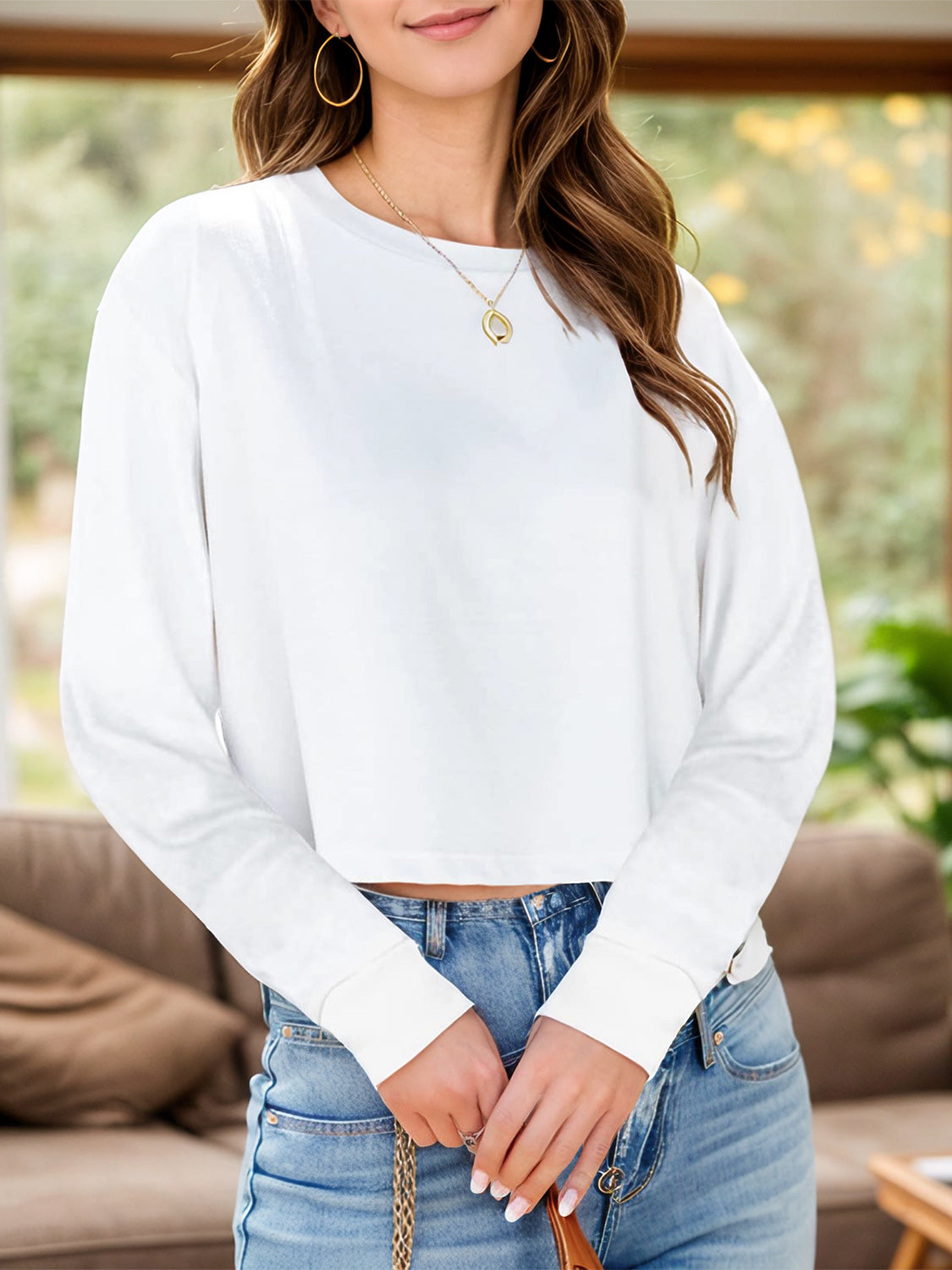 White cropped crewneck long sleeve top with cuffed sleeves, styled with jeans.